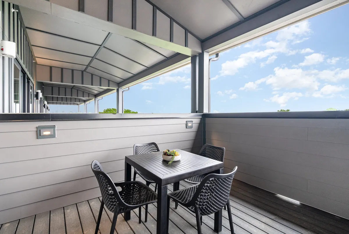 An inviting exterior balcony dining area with a table, four black chairs, a decorative plant centerpiece, and a spacious view. The ambiance is casual and serene, ideal for enjoying meals outdoors under the stars.