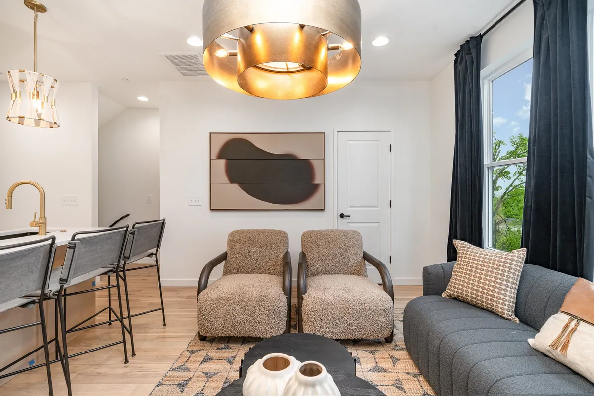 A stylish and comfortable lounge area with textured armchairs, a cozy couch, a modern chandelier, and artwork on the wall. The space is arranged to foster conversation, relaxation, and group activities, embodying a warm, welcoming atmosphere.