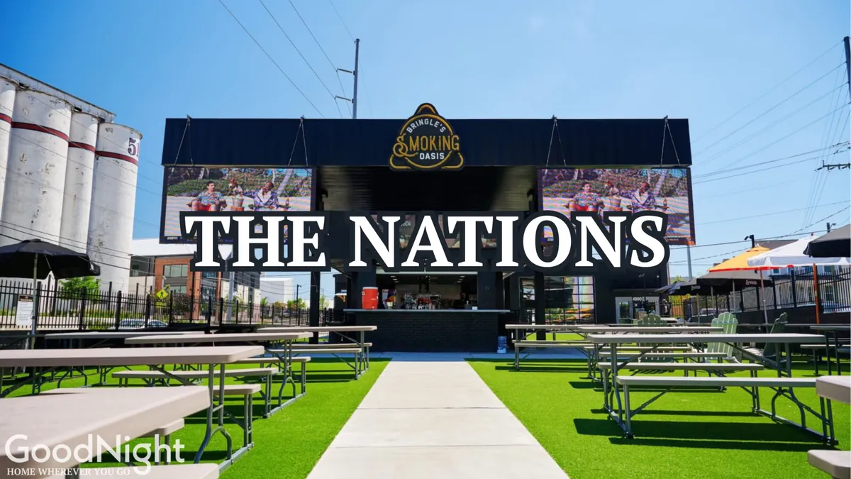 A lively exterior shot of 'THE NATIONS' sign with a bustling outdoor seating area and food service zone, capturing the neighborhood’s vibrant atmosphere. The scene includes people dining, socializing, and enjoying the festive environment, illustrating the local area’s appeal for group outings and offsite activities.