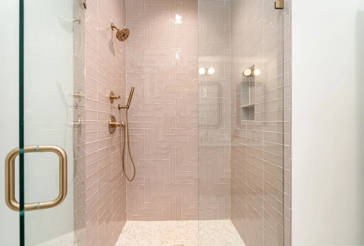 A luxurious bathroom with a herringbone tile pattern, gold fixtures, and a glass-enclosed shower. The ambiance is spa-like, providing a space for relaxation and indulgence.
