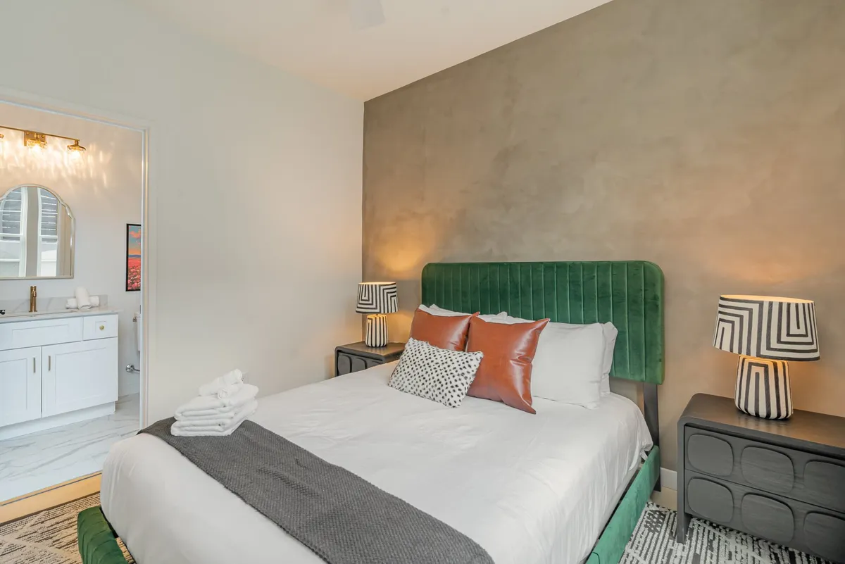 This image features a bedroom with a green upholstered headboard, decorative pillows, and stylish bedside lamps. The bed looks plush and inviting, with a contemporary design that feels both cozy and modern.
