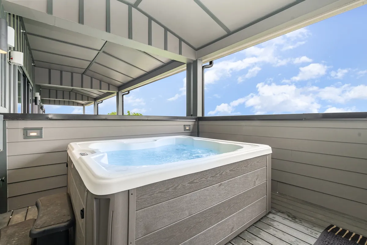 A serene rooftop scene featuring a bubbling hot tub set against open railings, with expansive views of the sky and cityscape beyond. The inviting water and unobstructed vista make this a standout amenity for relaxation and socializing above it all.