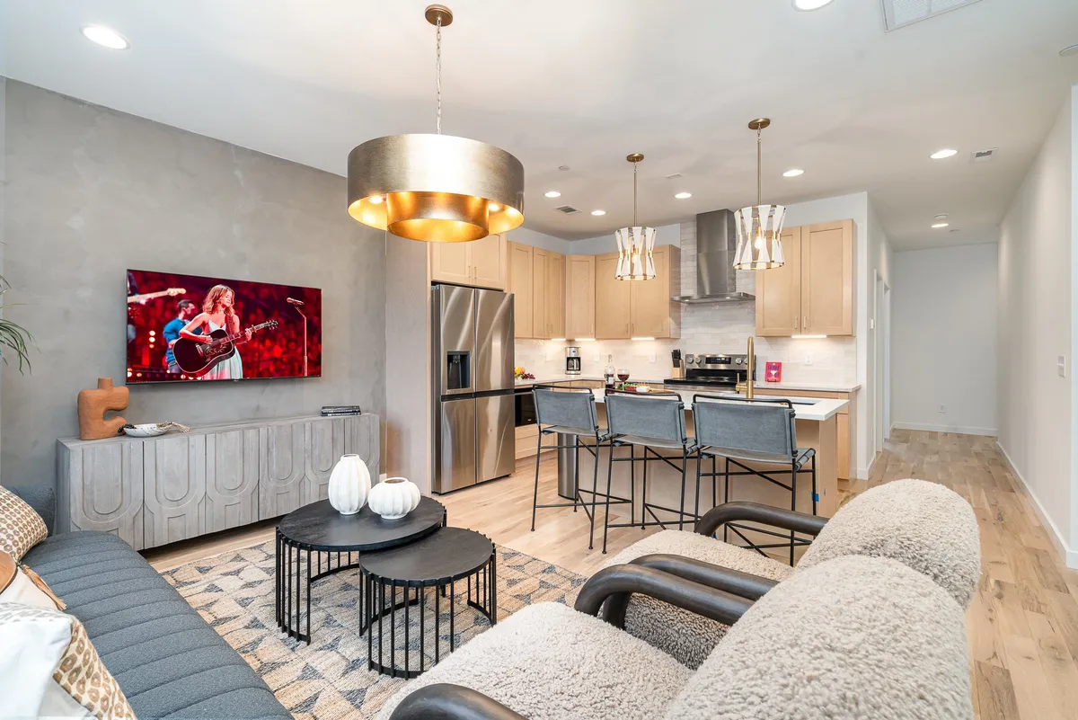The image showcases a bright and modern open-concept living space, featuring a comfortable sofa, a stylish coffee table, a sleek kitchen island, and a large smart TV. The setting is designed for both relaxation and gatherings, inviting guests to unwind, entertain, or enjoy cozy nights in. The room's layout emphasizes communal experiences, making it ideal for large groups or family celebrations.
