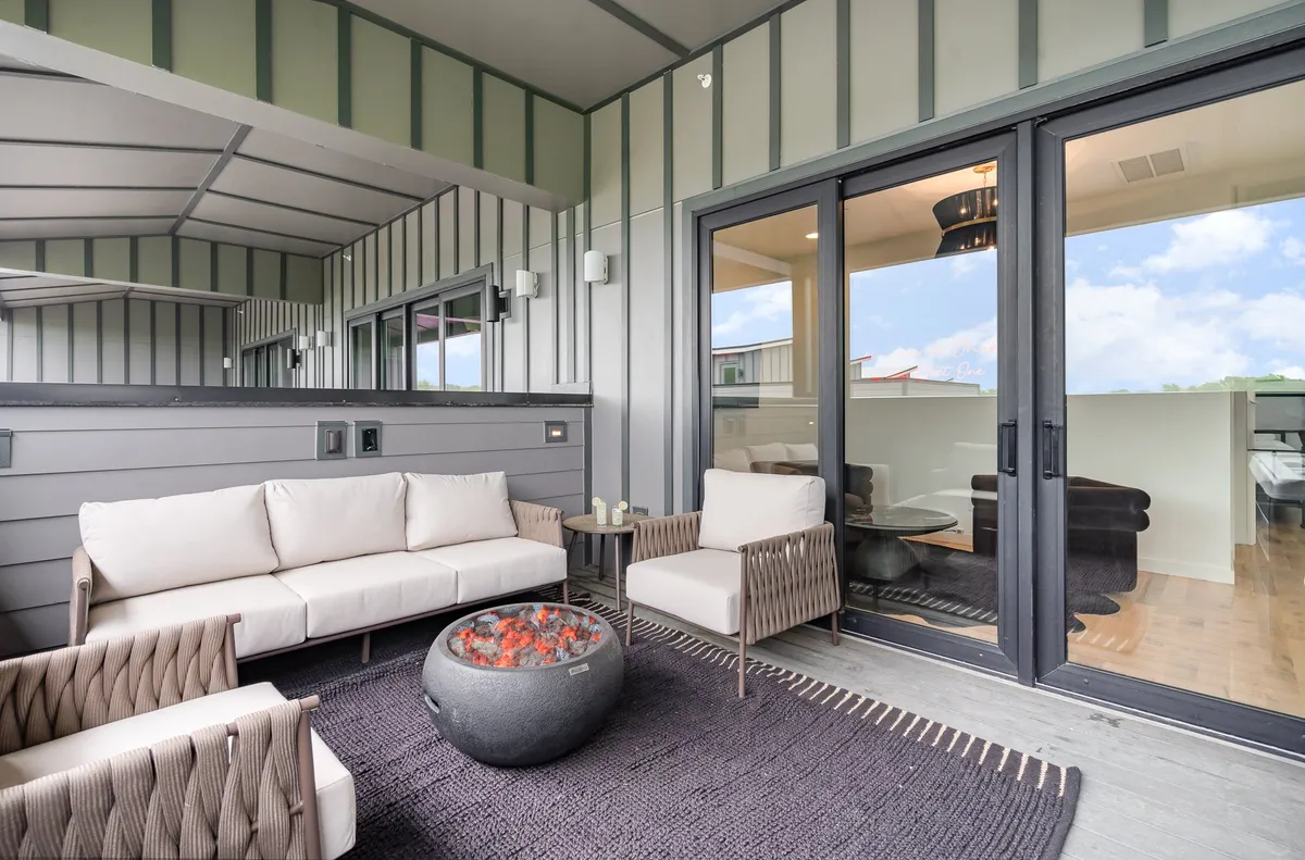 An outdoor seating area featuring a cozy fire pit, arranged with comfortable chairs and easy access to the indoor living spaces through glass doors. The ambiance is intimate and inviting, ideal for evening gatherings or casual discussions under the open sky.