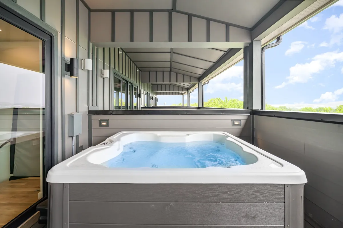 An inviting rooftop scene featuring a hot tub on the surrounding balcony, clear sky overhead, and ample space for relaxing and socializing. This outdoor area is ideal for group gatherings and enjoying views, day or night.